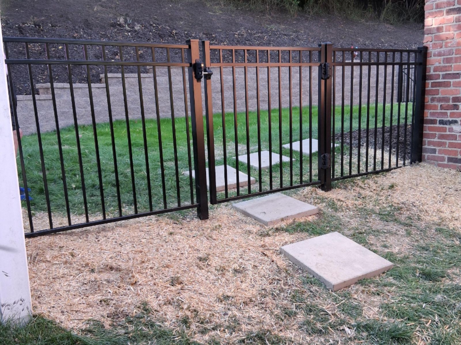 A black aluminum fence and gate with stepping stones, installed by M.S.S Landscaping