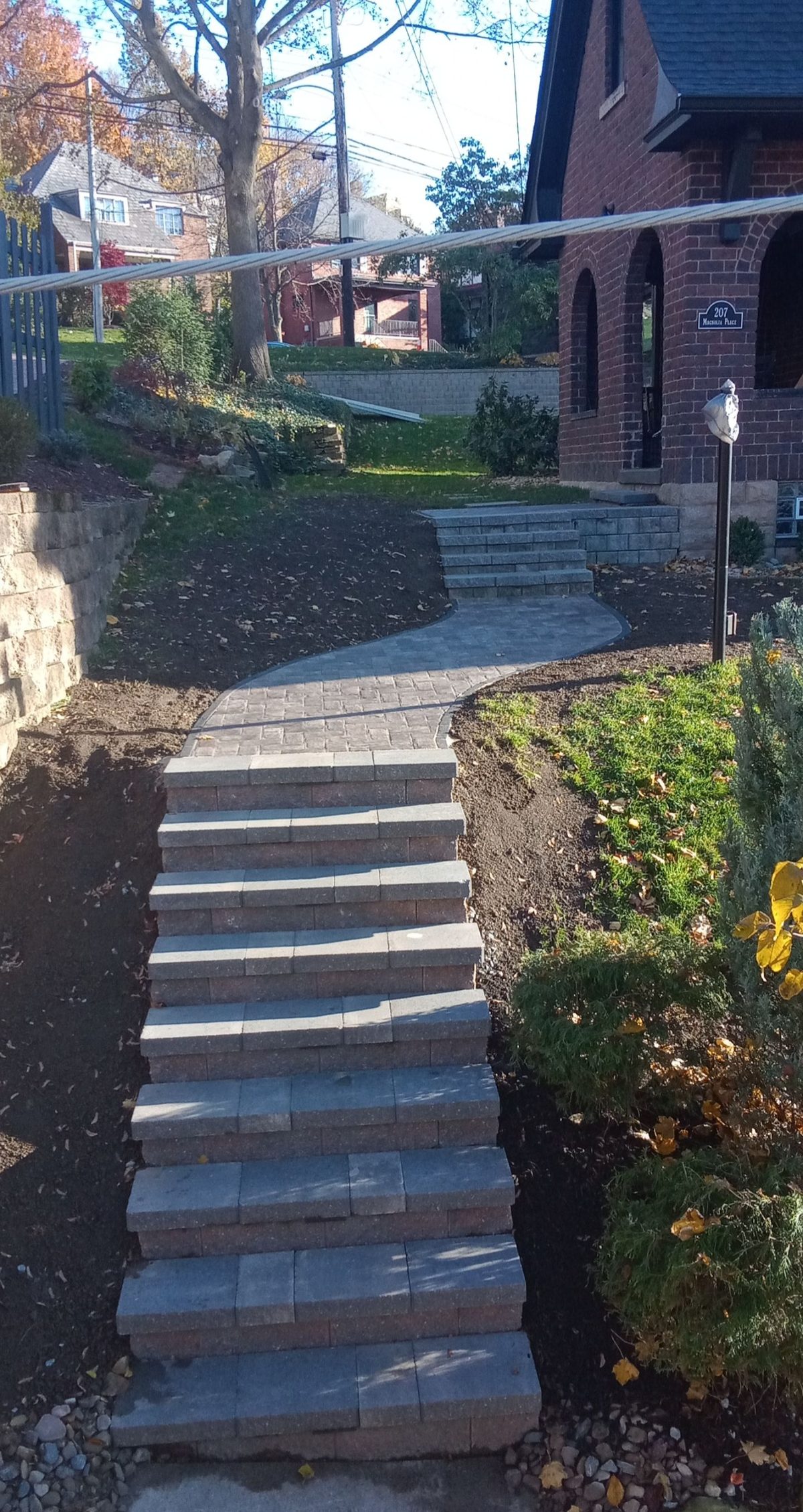 A curved paver walkway and block steps up to a brick house, built by M.S.S Landscaping