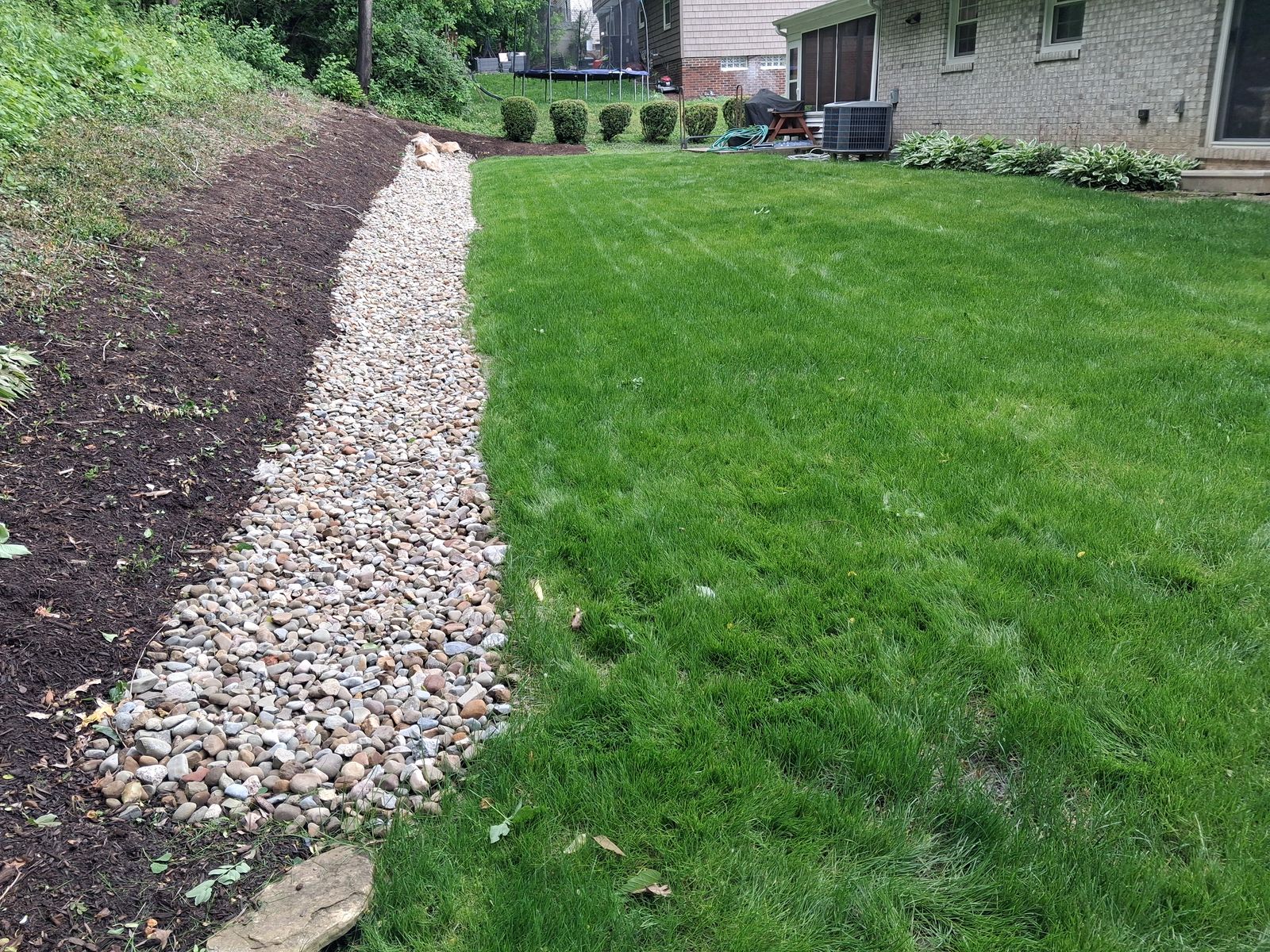 A river rock drainage channel between a mulched slope and the lawn