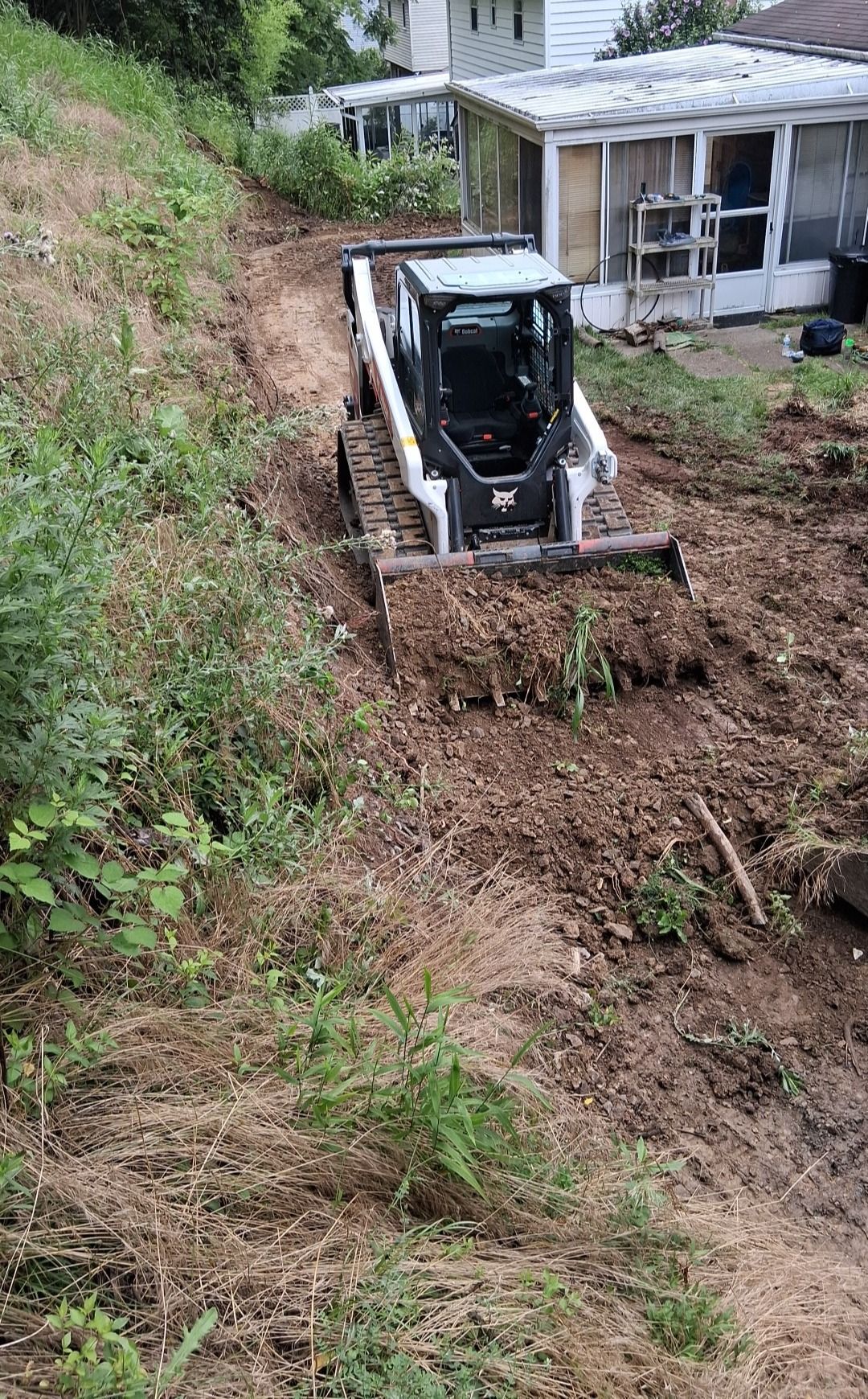 An M.S.S Landscaping skid steer cutting and grading a back yard slope